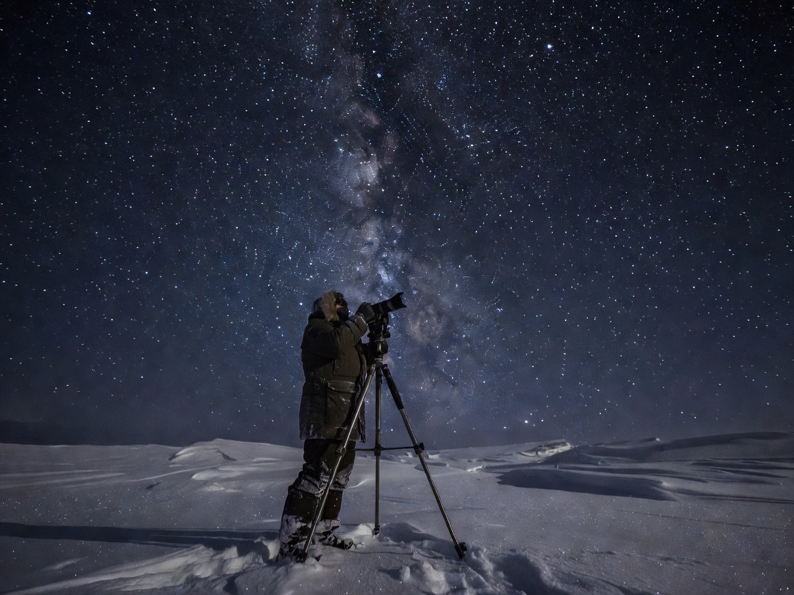 Photographer with sturdy metal tripod pointed toward a dark star-filled Arctic sky